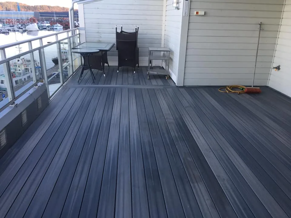 Ny terrasse i grå kompositt med glassrekkverk og utsikt mot sjøen